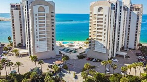 A high-rise hotel with a pool, located near a beach with clear blue waters.