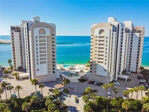 A high-rise hotel with a pool, located near a beach with clear blue waters.