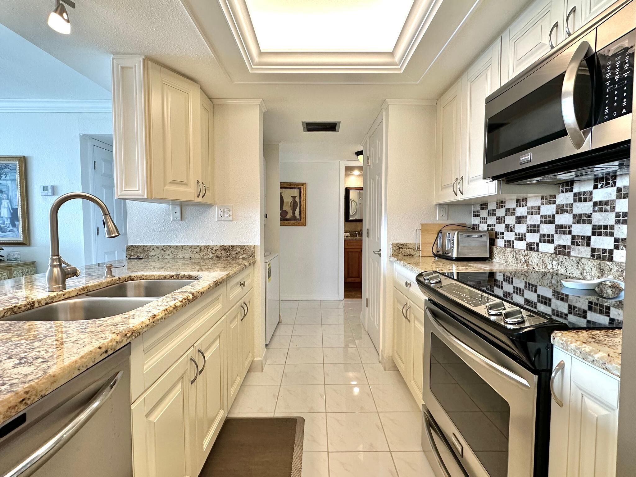 Una cocina moderna con encimeras de granito, electrodomésticos de acero inoxidable y armarios blancos.