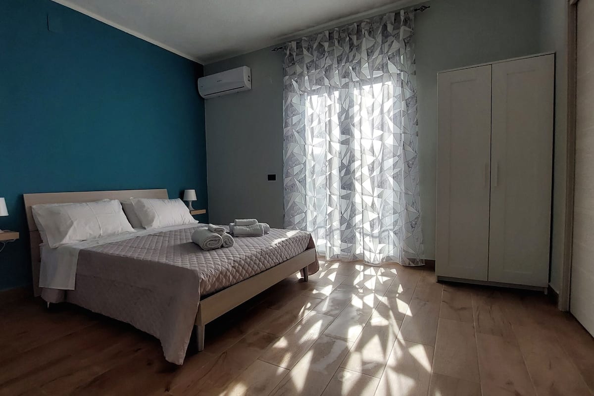 A bedroom with a bed, bedside lamps, a wardrobe, and a window with patterned curtains.