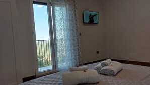 A hotel room with a bed, a window with a view of a balcony, and a painting on the wall.