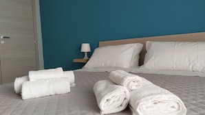 A neatly made bed with white linens and pillows, a bedside table with a lamp, and a teal-colored wall.