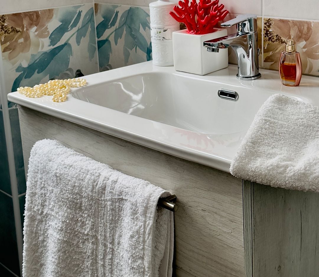 Une salle de bain avec un lavabo blanc, un miroir, un objet de décoration en corail rouge et un flacon de savon.