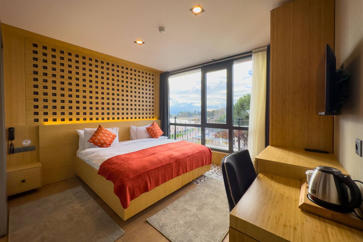 A modern hotel room with a large bed, a desk, a kettle, and a TV.