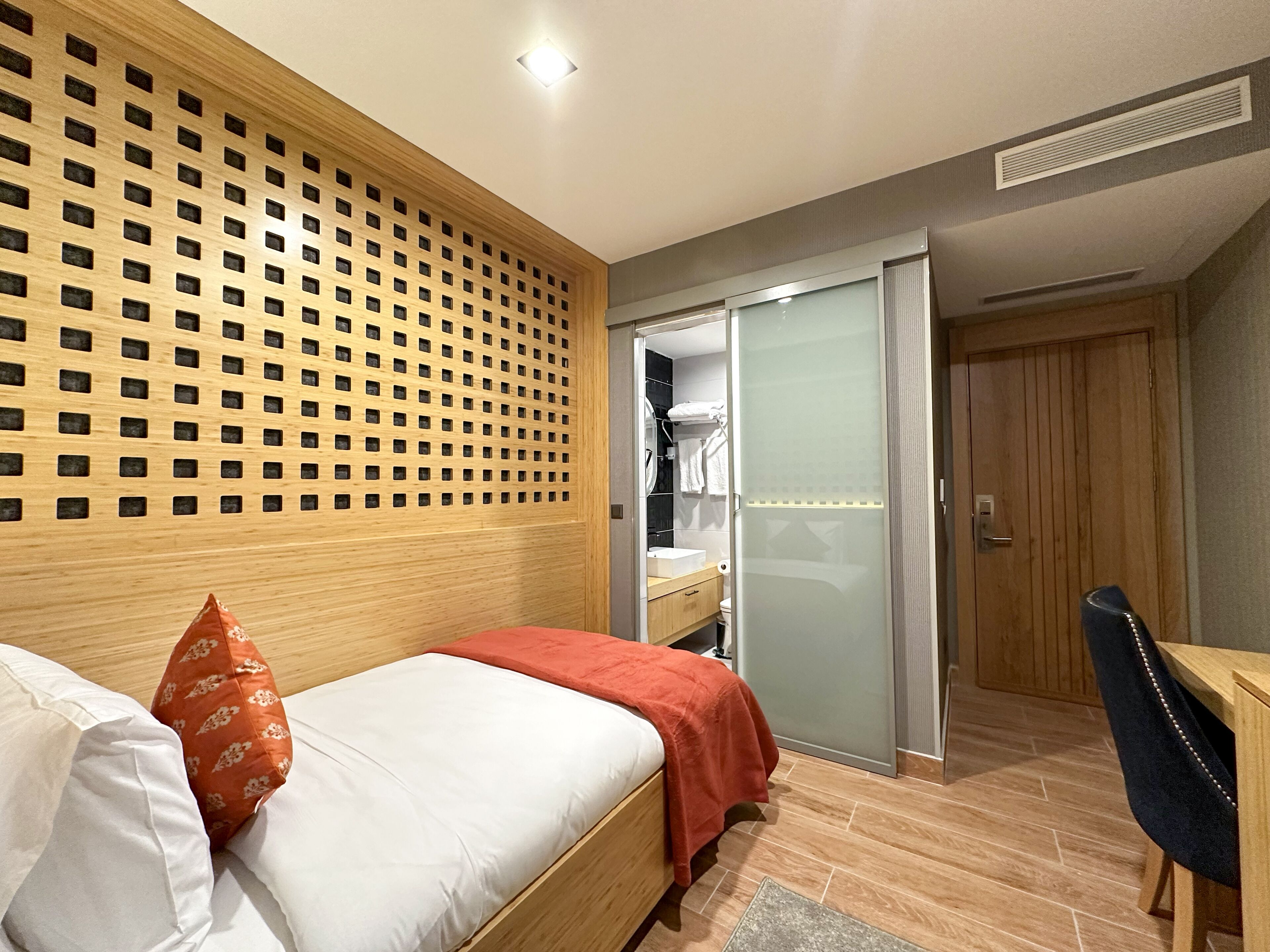Un dormitorio moderno con cabecera de madera, cama con ropa de cama blanca y roja, un escritorio y un vestidor con espejo.