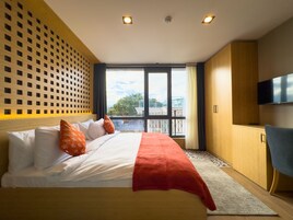 Una habitación de hotel moderna con una cama grande, un televisor y un balcón con vista a la ciudad.