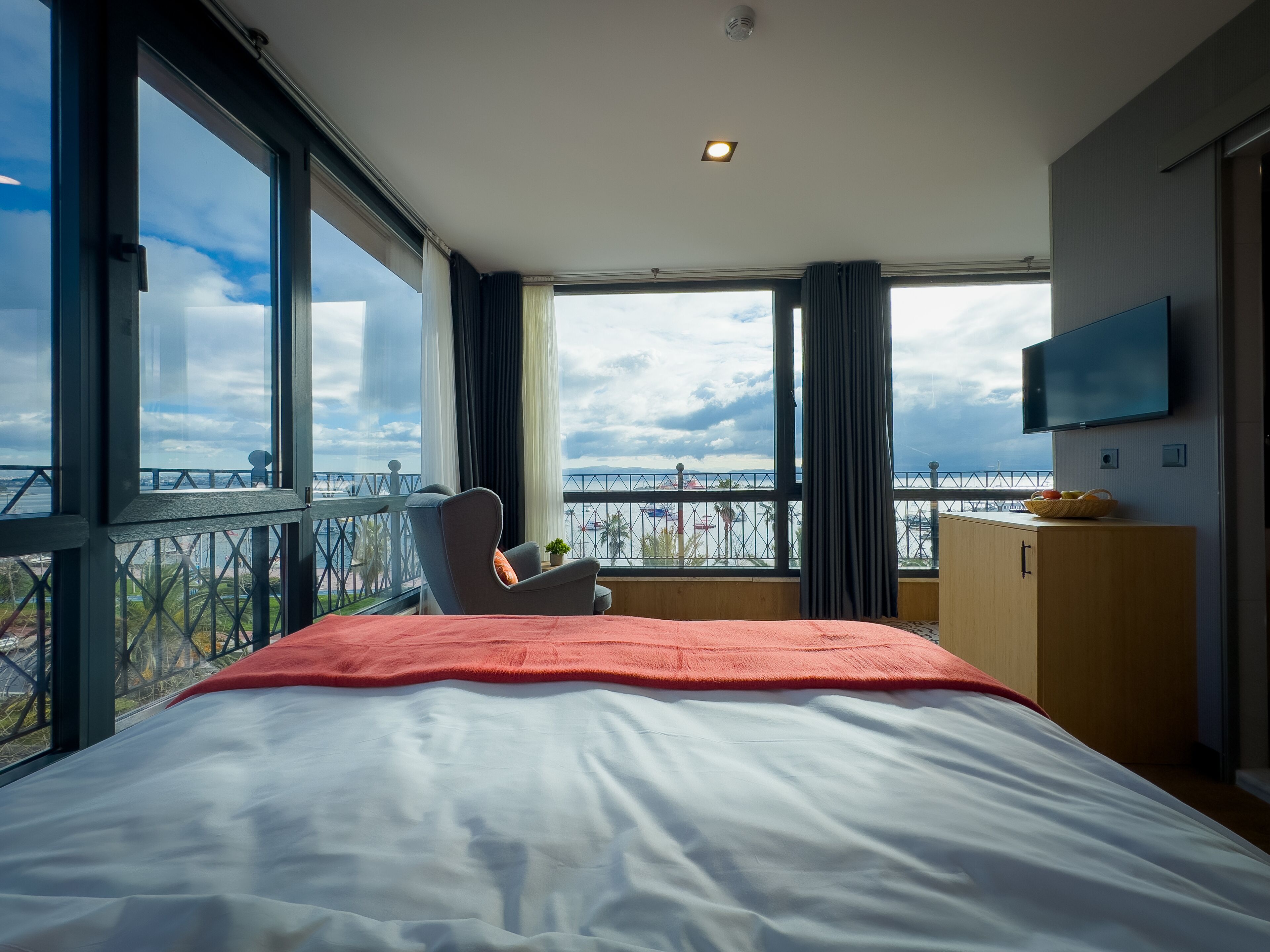Habitación de hotel con una cama grande, una silla, un televisor y un balcón con vistas a la ciudad.