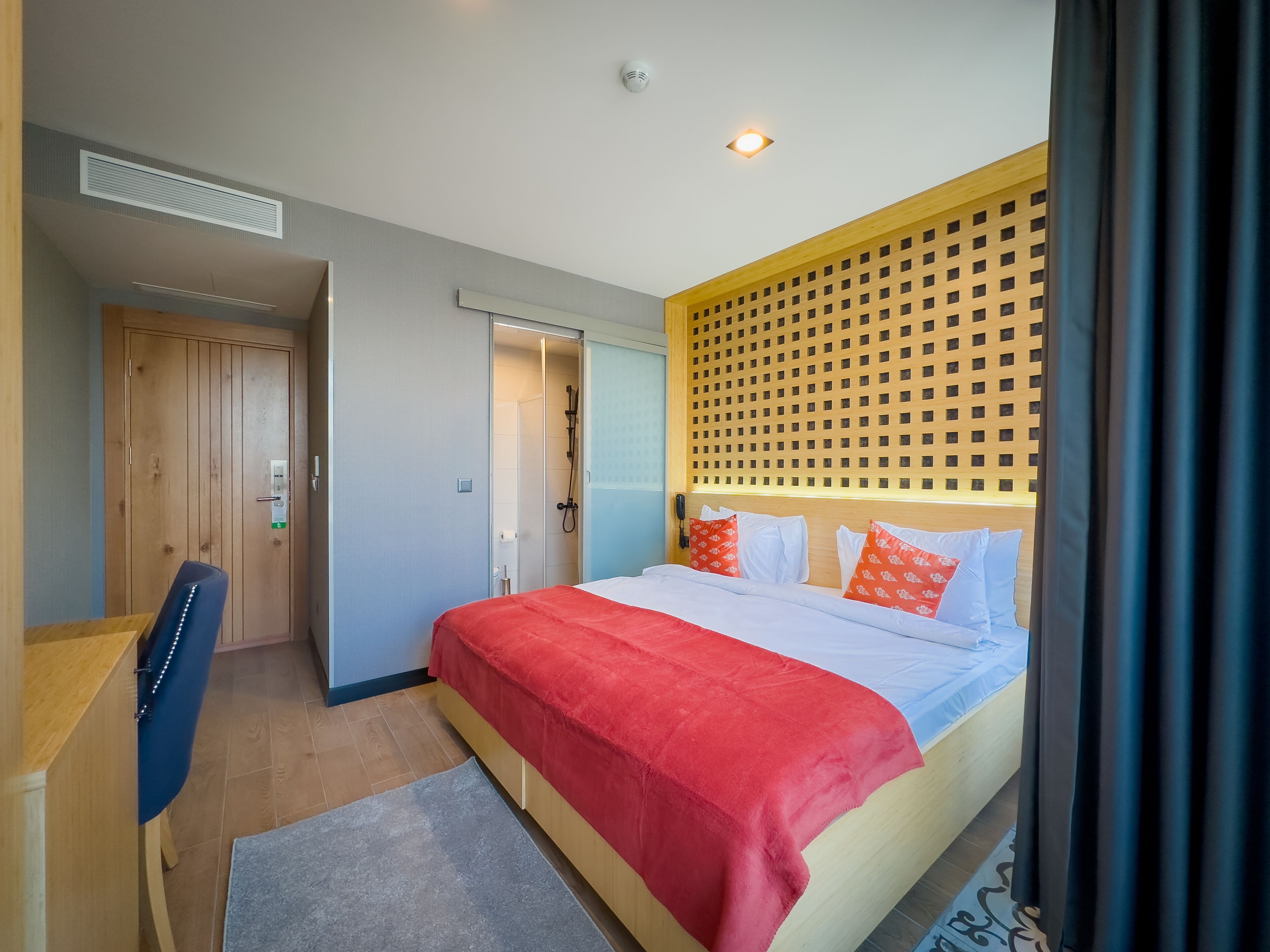 Habitación de hotel con cama, escritorio, ducha y pared divisoria de madera.