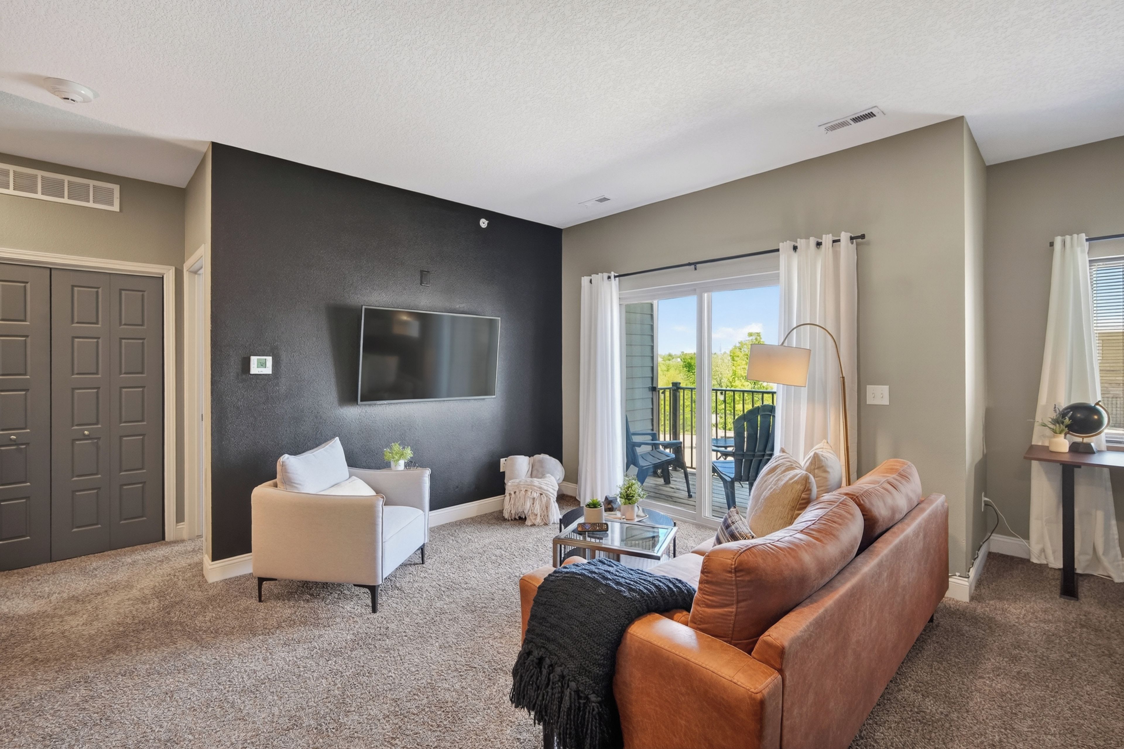 Una sala de estar con una pared de acento oscura, un televisor de pantalla plana, un sofá de cuero, un sillón blanco y una mesa de centro de vidrio.