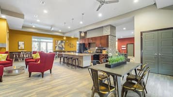 Un salon moderne avec des canapés rouges, un coin repas doté d’une longue table et une cuisine avec des meubles en bois.