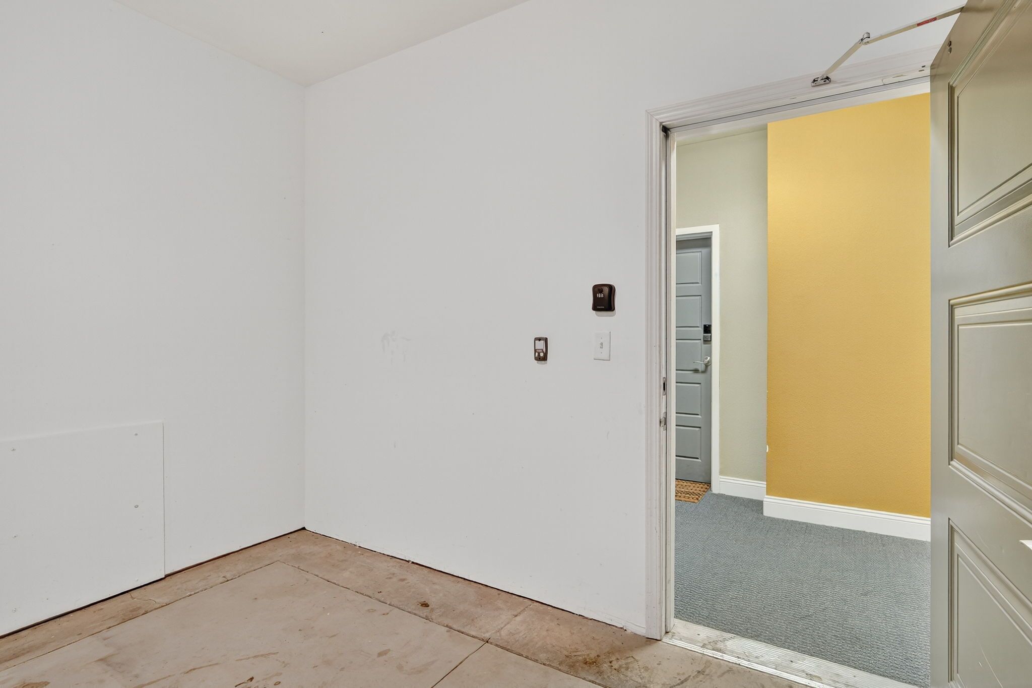 A room with a white door, a light switch, and a small electrical outlet on the wall.