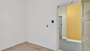 A room with a white door, a light switch, and a small electrical outlet on the wall.