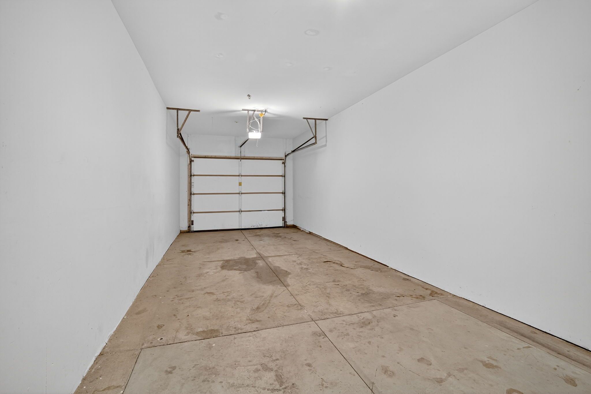 A room with white walls, a concrete floor, and a ceiling with exposed beams and a single light fixture.