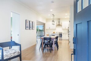 Una cocina moderna con armarios blancos, una mesa de comedor de madera y una puerta azul.