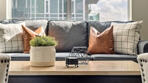 A modern living room with a grey sofa, a small potted plant, and a geometric metal sculpture on a wooden coffee table. - Near Stampede/ BMO Centre w Prkg & Gym (+18) (Calgary)