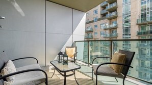 A balcony with two chairs, a small table, and a glass railing overlooking a high-rise building. - Near Stampede/ BMO Centre w Prkg & Gym (+18) (Calgary)