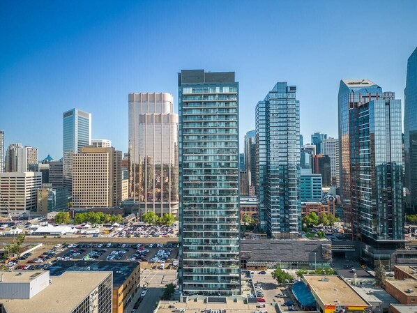 A cityscape with modern high-rise buildings, a parking lot, and a clear blue sky. - Modern Comfort with Views, Parking, Office & AC (Calgary)