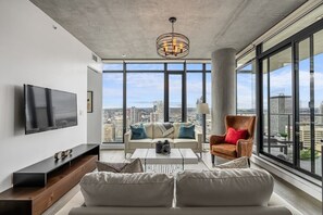 A modern living room with a large TV, a sofa, a coffee table, and a chair. - Modern Comfort with Views, Parking, Office & AC (Calgary)