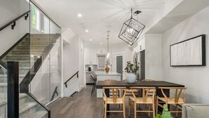 A modern kitchen with a dining area, featuring a staircase with glass railings, wooden flooring, and a hanging pendant light. - Modern Mediterranean 4BR near Downtown w/ Cable (Calgary)