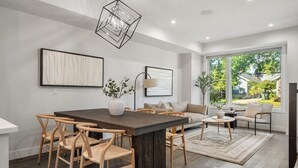 A modern living room with a dining area, large windows, and a view of the outdoors. - Modern Mediterranean 4BR near Downtown w/ Cable (Calgary)