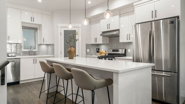 A modern kitchen with white cabinetry, a stainless steel refrigerator, a central island with bar stools, pendant lighting, and a built-in oven. - Modern Mediterranean 4BR near Downtown w/ Cable (Calgary)
