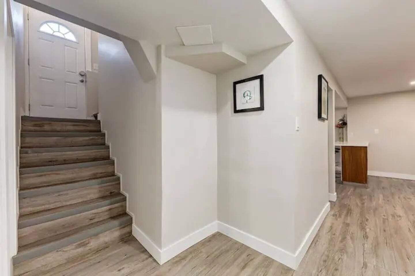 A hallway with a wooden staircase, white walls, and a wooden floor.