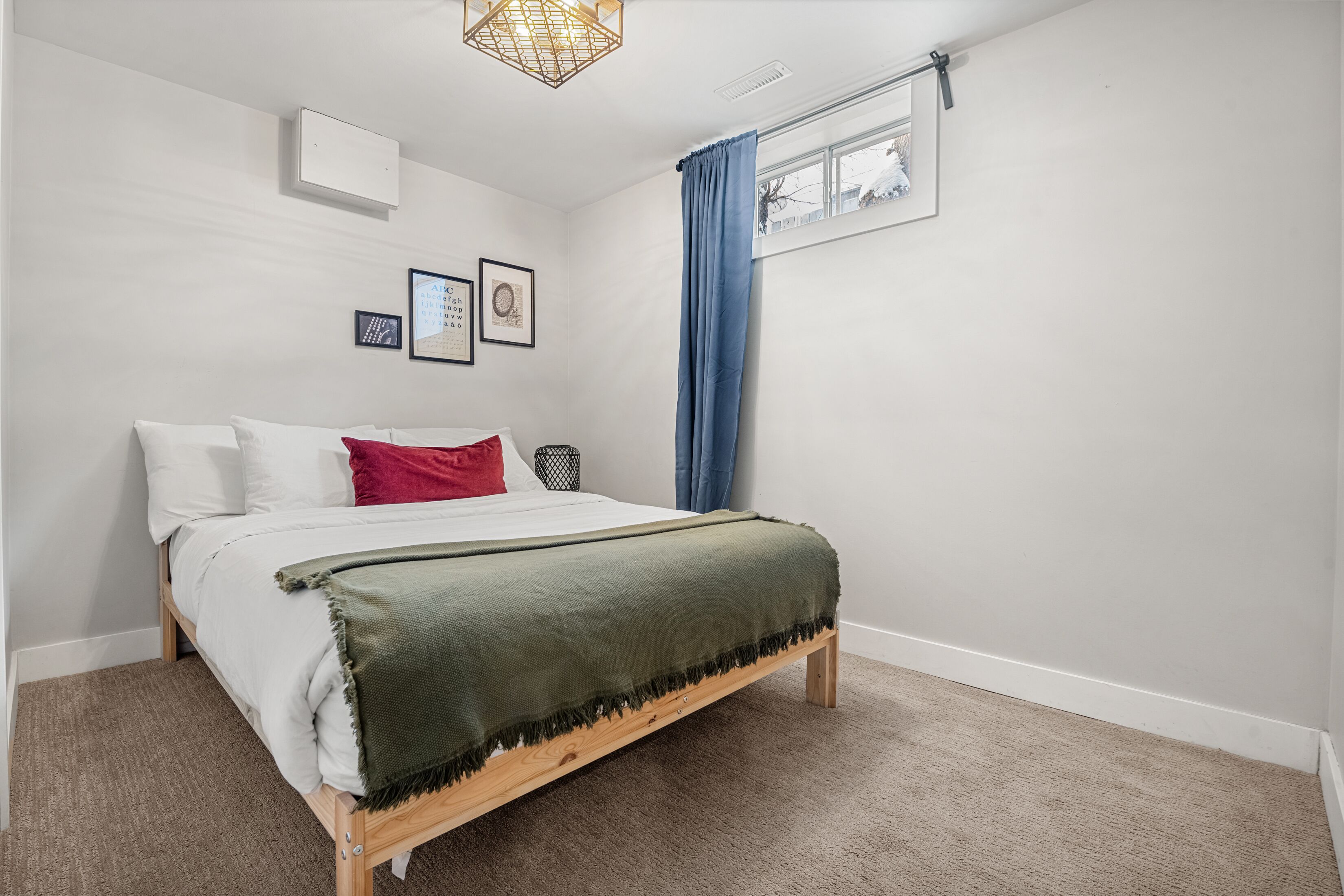 A bedroom with a bed, a window with blue curtains, a picture frame, and a light fixture.