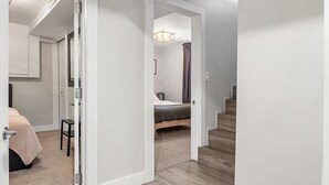 Ein Korridor mit Holzboden, der zu einem Schlafzimmer mit einem Bett und einem Sessel führt.