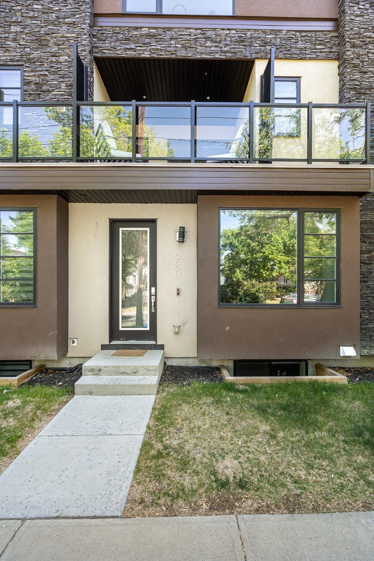 Een modern huis met twee verdiepingen, een stenen gevel, grote ramen en een voordeur met een brievenbus.