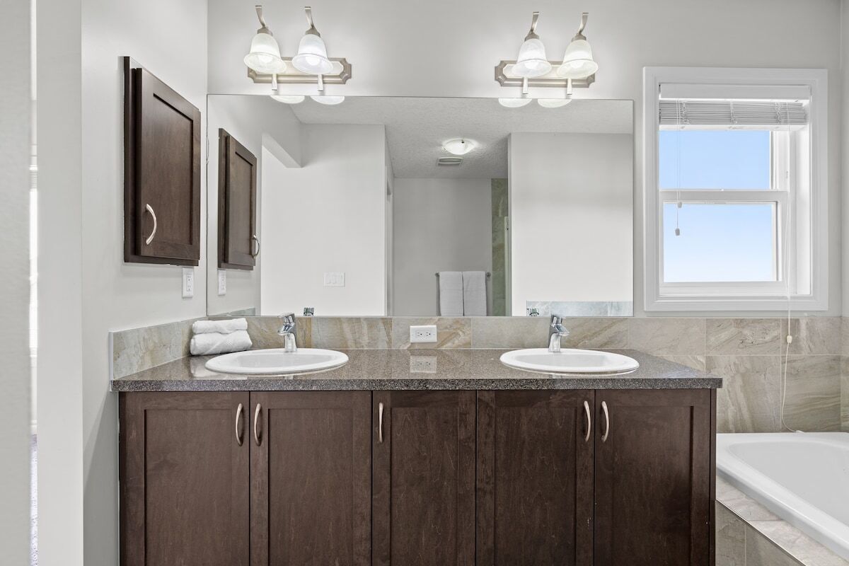 A bathroom with two sinks, dark wood cabinets, a large mirror, and a window with blinds.