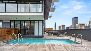 Piscina no terraço com deck de madeira, espreguiçadeiras e vista para o horizonte da cidade.