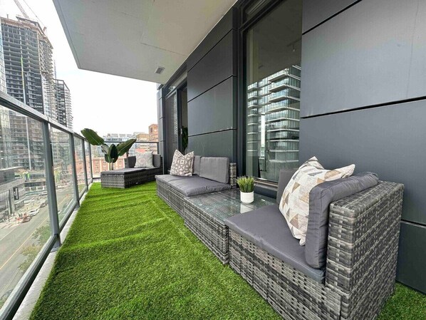 A balcony with artificial grass, wicker furniture, and a view of the cityscape.