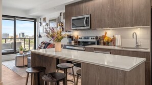 A modern kitchen with a large island, dark wood cabinets, and a city view. - Howdy! 1BR Western Theme w Rooftop Patio & AC (Calgary)