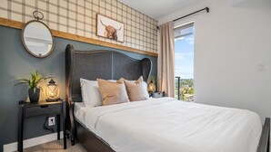 A bedroom with a large bed, a headboard with a woven design, a bedside table with a lamp, a mirror, and a framed picture on the wall. - Howdy! 1BR Western Theme w Rooftop Patio & AC (Calgary)