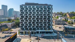 A multi-story building with a grid of balconies, surrounded by a parking lot and other buildings. - Howdy! 1BR Western Theme w Rooftop Patio & AC (Calgary)