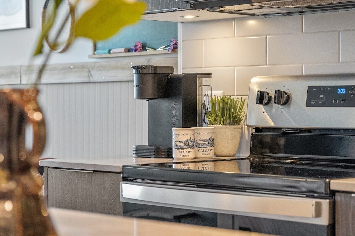 A modern kitchen with a stainless steel range hood, a digital clock displaying 3:08, and two potted plants on the counter.