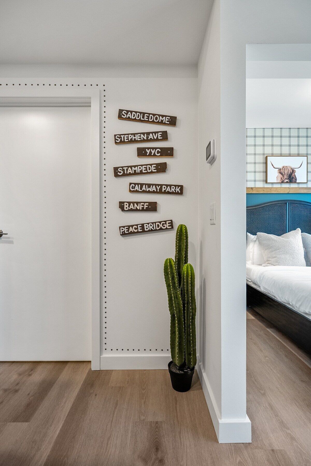A modern room with a white door, a cactus plant, and a bed with white bedding.