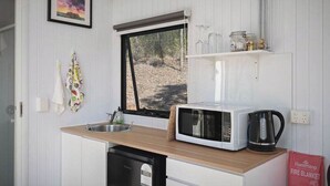 Una cucina compatta con forno a microonde, bollitore e finestra vista alberi.