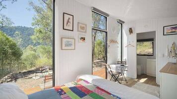 A bedroom with a large bed, a view of the outdoors, a small kitchenette, and a dining area.