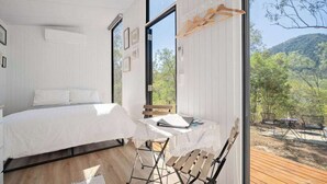 Una camera da letto con un letto, un tavolo con un portatile e vista su una terrazza e alberi.