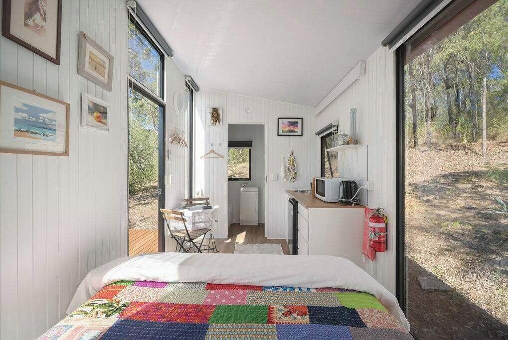 A bedroom with a colorful quilt, a small kitchenette, and a view of the outdoors.