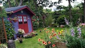 Une terrasse en bois agrémentée de plantes en pot et d’un petit abri de jardin.