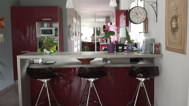 Une cuisine moderne dotée d’un îlot central, de tabourets de bar, de luminaires suspendus et d’une horloge murale.