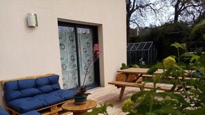 Un espace extérieur aménagé avec un canapé et des tables, un pot de fleurs et une fenêtre ornée de rideaux à motifs.
