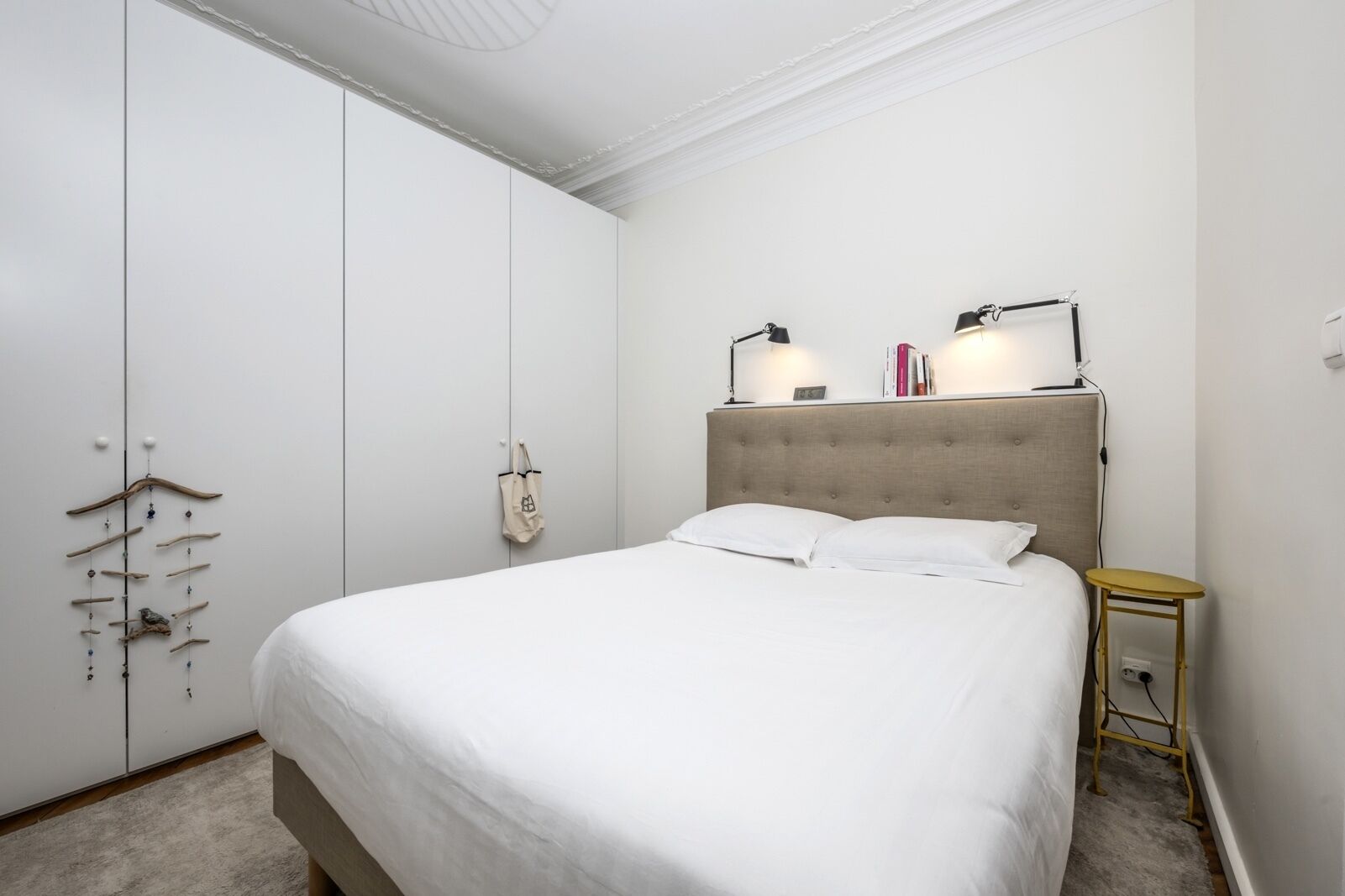 A bedroom with a large bed, a wardrobe, a bedside table with a lamp, and a small table with a lamp.
