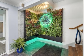 Un intérieur moderne agrémenté d’un mur végétal vertical, d’une enseigne au néon et d’un escalier en bois.