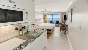 A hotel room with a kitchenette, a bed, a balcony with a view, and a dining area.