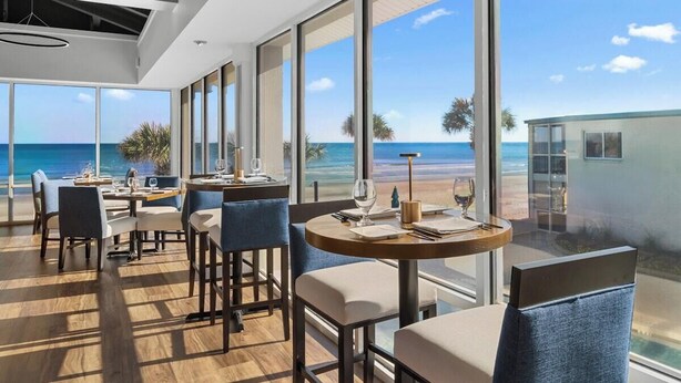 A modern dining area with large windows, wooden flooring, and a view of the ocean.