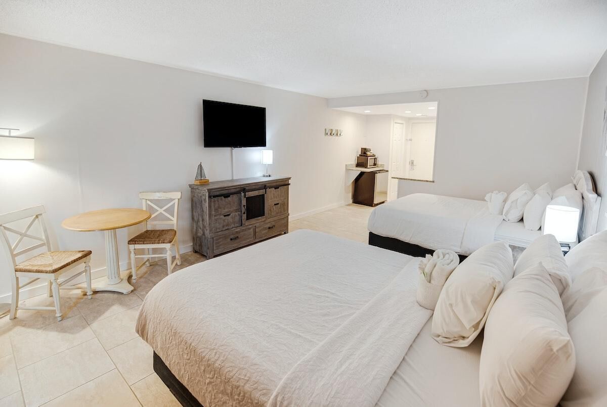 A hotel room with a large bed, a desk with a chair, a television mounted on the wall, and a small table.