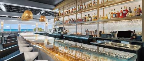 A bar area with a long counter, multiple shelves of liquor bottles, and seating with a view.